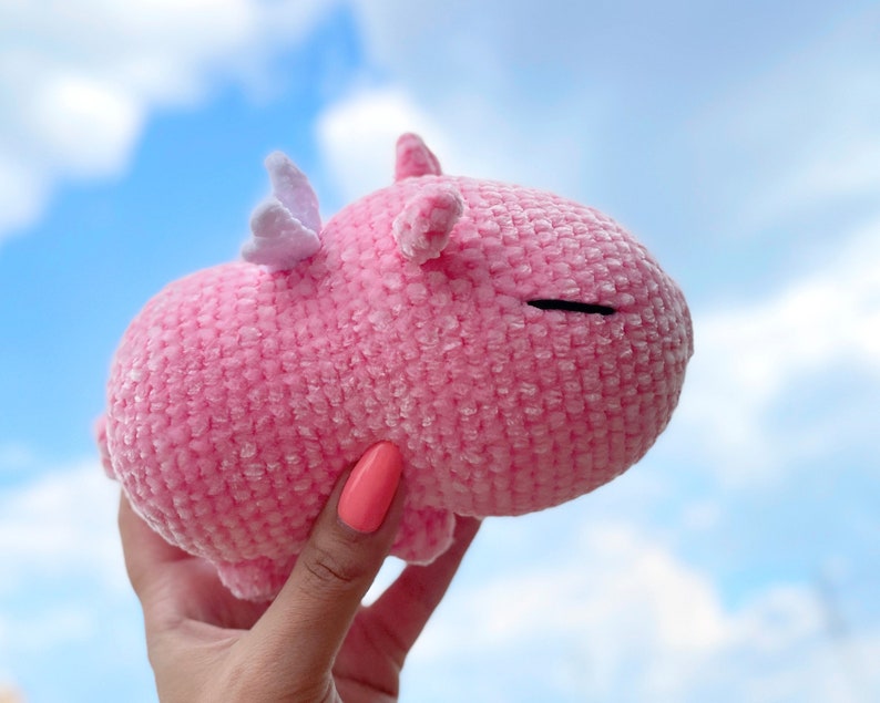 K&ouml;nnte beinhalten: Ein rosa geh&auml;keltes Stofftier mit einem wei&szlig;en Horn und einem geschlossenen Auge. Das Tier wird in einer Hand gehalten.