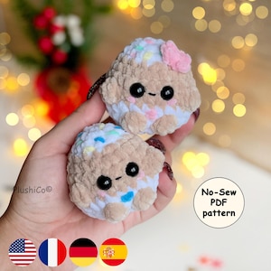 May include: Two small, round, crocheted plush toys made of soft, tan yarn with white accents and colorful speckles. Each plush features large black safety eyes, a tiny embroidered mouth, and pink blush marks. One has a small pink bow on top.
