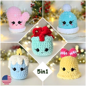 May include: A collection of five plush crochet ornaments featuring a pink mitten, a blue winter hat with a white pom-pom, a light green gift box with a red bow, a blue candle with a yellow flame, and a yellow bell with a pink bow.
