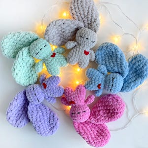 May include: Six crocheted plush bunny toys with embroidered eyes and hearts. The bunnies are in various colors, including light blue, pink, purple, and gray.