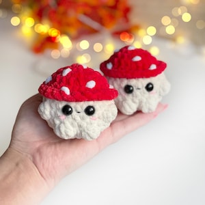 May include: Two adorable crochet mushroom figures. Each mushroom has a red cap with white spots, a cream-colored body, and black eyes. The mushrooms are small, soft, and have a cute, friendly appearance. They are likely handmade and suitable for decorative purposes.