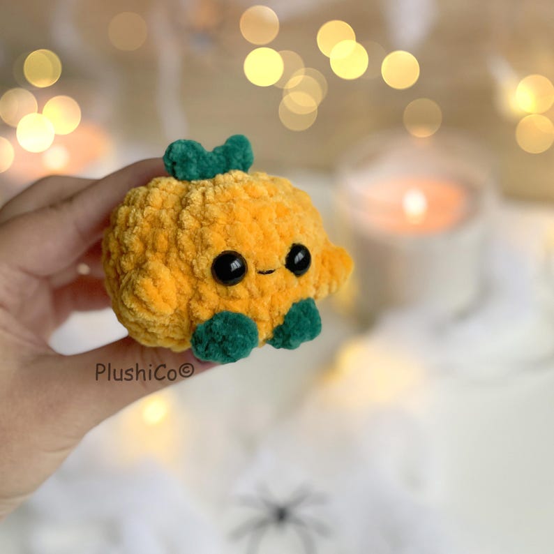 May include: A handmade, plush pumpkin toy with a smiling face, black eyes, and green accents. The pumpkin is orange and has a green stem and green feet. The toy is soft and cuddly, perfect for fall decor or as a gift.