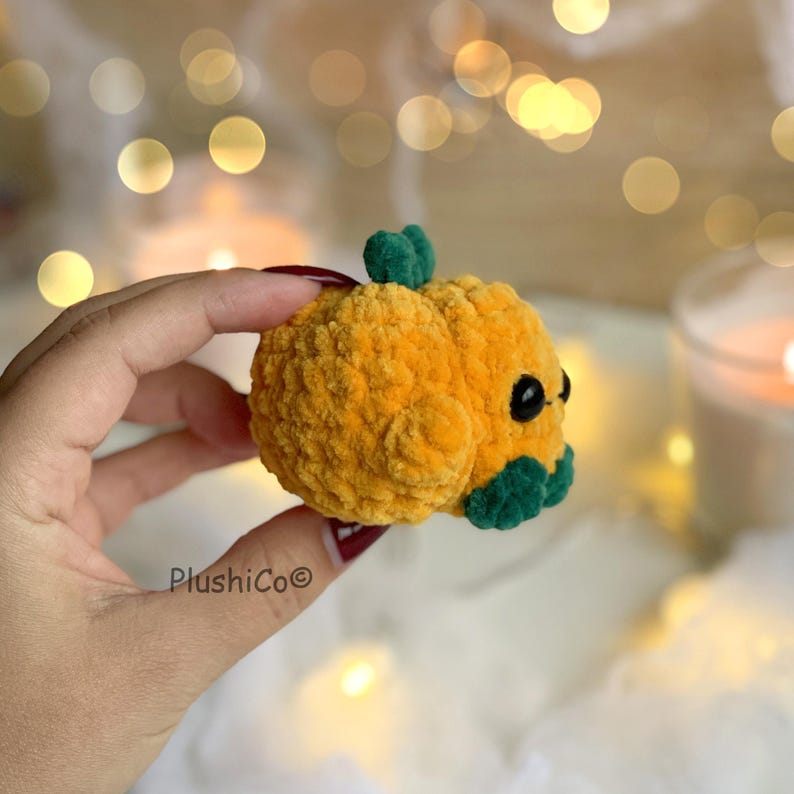 May include: A small, plush orange pumpkin with green leaves and black eyes. The pumpkin is handmade and has a soft, textured appearance. The product is a cute, decorative item, perfect for fall or Halloween.