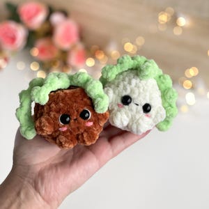 May include: Two small, round, plush crochet figures resembling vegetables. One is brown and the other is white, both featuring light green textured tops, large black safety eyes, and small pink embroidered cheeks on their soft, fuzzy surfaces.