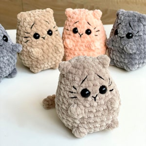 May include: Five crocheted plush cat toys in different colors, including gray, brown, beige, and peach. The cats have black eyes and embroidered whiskers.