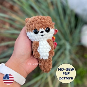 May include: A crocheted brown and white otter plush toy with large black eyes. The toy is being held in a hand. The text "NO-SEW PDF pattern" is visible in the image.