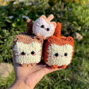 May include: Three crocheted plush cat toys in different colours. The largest cat is orange and brown, the middle cat is brown and white, and the smallest cat is peach and white.