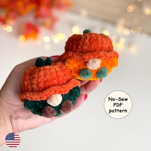 May include: Two small, round, crocheted plush figures resembling pumpkins with hats. One figure has a dark green base with brown feet, while the other has an orange base with green feet. Both feature a beige nose and a textured, orange pumpkin-shaped top.