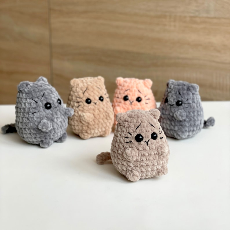May include: Five crocheted cat toys in different colors, including gray, brown, and peach. The cats have black eyes and whiskers.
