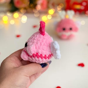 Peut inclure: Une petite peluche crochet&eacute;e douce en forme de poisson rose avec une nageoire rose fonc&eacute; sur le dessus, des nageoires lat&eacute;rales blanches et des yeux en perles noires. La peluche a une surface en laine textur&eacute;e et une bande rose fonc&eacute;.