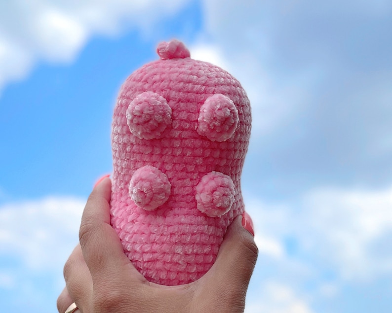 K&ouml;nnte beinhalten: Ein rosa geh&auml;keltes Stofftier mit einer strukturierten Oberfl&auml;che und vier gro&szlig;en, runden, flauschigen Noppen.