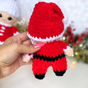 Puede incluir: Un mu&ntilde;eco de Pap&aacute; Noel de crochet con un gorro rojo, ribete blanco y un traje rojo y negro. El mu&ntilde;eco lleva una peque&ntilde;a bolsa blanca.
