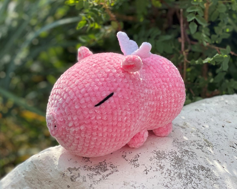 K&ouml;nnte beinhalten: Ein rosa geh&auml;keltes Stofftier mit einem wei&szlig;en Horn und geschlossenen Augen. Das Tier liegt auf einem wei&szlig;en Stein.