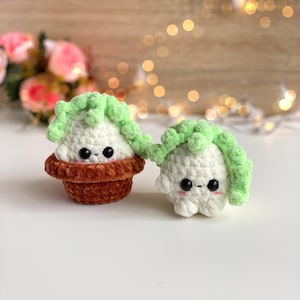 May include: Two small, round, crocheted plush figures made of soft white yarn with light green textured tops. One figure sits inside a brown crocheted pot, while the other stands beside it. Both have black bead eyes and small pink stitched cheeks.