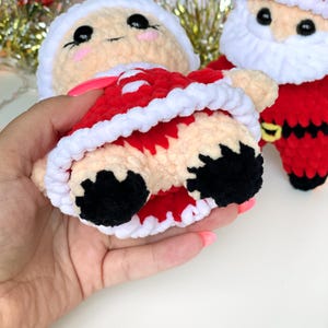 Puede incluir: Un juguete de peluche tejido a crochet vestido de Pap&aacute; Noel. El juguete tiene un atuendo rojo y blanco con un ribete de piel blanca. El juguete tiene hilo negro para los ojos y hilo rosa para la nariz.