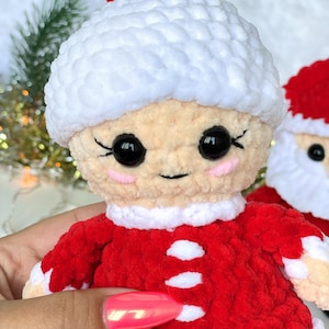 Puede incluir: Un adorno navide&ntilde;o de crochet de una mujer con un sombrero blanco y un vestido rojo y blanco. El adorno tiene una cara sonriente con ojos negros y mejillas rosadas.