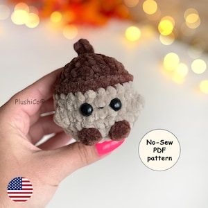 May include: A crocheted acorn plushie in shades of brown and beige, featuring large black eyes and small brown feet. The plushie is held in a hand, with the text "No-Sew PDF pattern" visible. The Plushico logo is also visible.