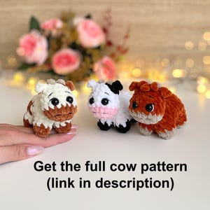 May include: Three handmade crochet cow figurines in white, brown, and orange. The cows have large black eyes and are displayed on a white surface. Text at the bottom reads "Get the full cow pattern (link in description)".