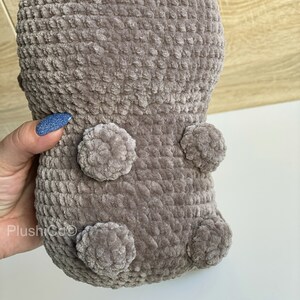 May include: A brown crocheted plush toy with a textured surface and four round, fluffy pom-poms.