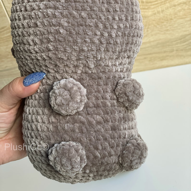 May include: A brown crocheted plush toy with a textured surface and four round, fluffy pom-poms.