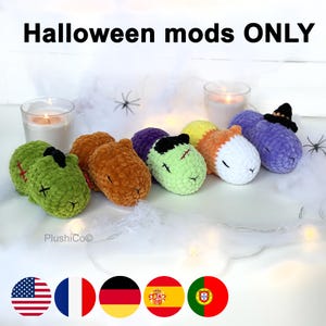 Pode incluir: Cinco brinquedos de pelúcia de crochê em diferentes cores e designs, incluindo um zumbi, uma abóbora, um monstro, um unicórnio e um vampiro. Os brinquedos estão dispostos em uma fila sobre uma superfície branca com velas e uma teia de aranha no fundo. Halloween mods ONLY.