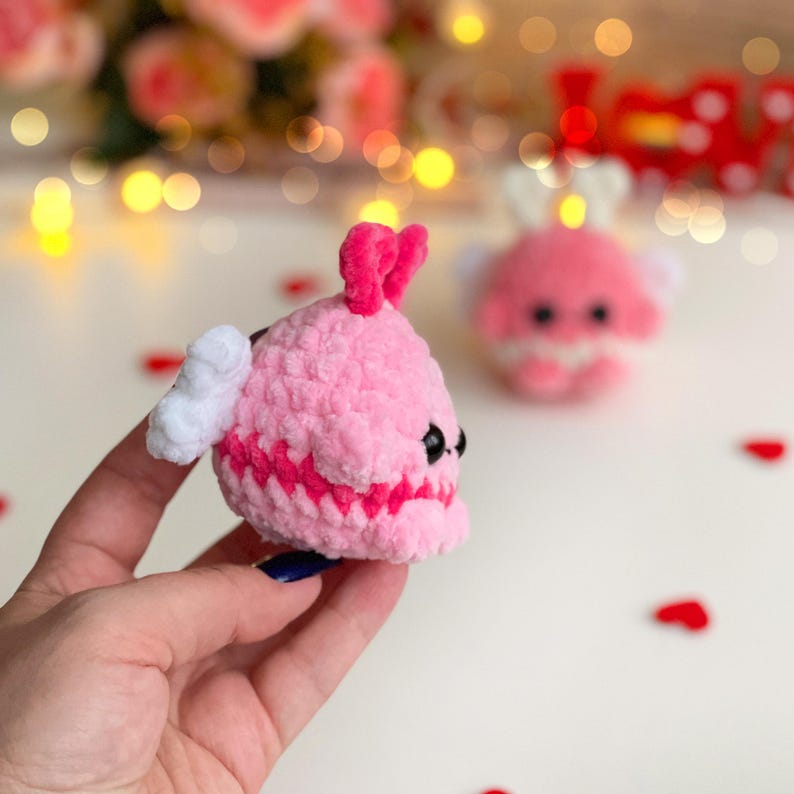 Peut inclure: Un petit jouet en peluche crochet&eacute;, rond et rose clair, avec une finition en fil textur&eacute;. Il pr&eacute;sente deux petites ailes blanches sur les c&ocirc;t&eacute;s, un d&eacute;tail en forme de c&oelig;ur rose vif sur le dessus et deux petits yeux en perles noires.