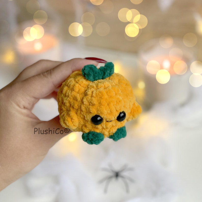 May include: A plush, orange pumpkin with a smiling face, green stem, and green feet. The handmade, crocheted pumpkin is a cute Halloween decoration. The product is made by PlushiCo.