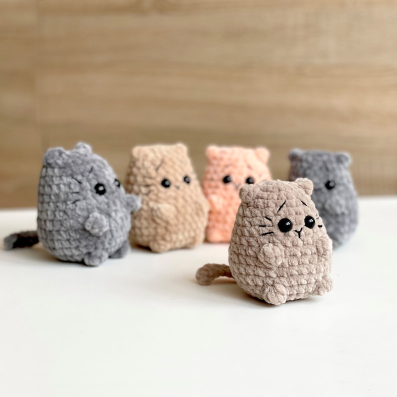 May include: Five crocheted plush cat toys in different colors, including gray, brown, and pink. The cats have black eyes and whiskers.