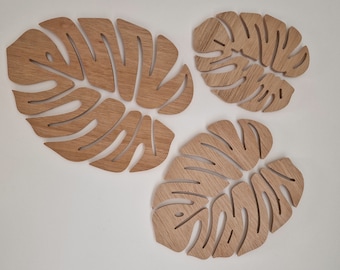 May include: Three wooden wall decor pieces shaped like monstera leaves. The leaves are different sizes and are made of light brown wood.