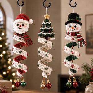 Pode incluir: Três ornamentos de crochê pendurados representando o Papai Noel, uma árvore de Natal e um boneco de neve. Cada figura tem uma longa cauda de fita branca em espiral decorada com pequenos flocos de neve bordados em verde e vermelho, terminando com duas pequenas bolas metálicas.