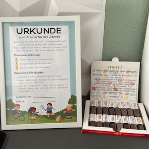 Könnte beinhalten: Eine weiße gerahmte Urkunde mit einer bunten Illustration von Kindern, die Sport treiben. Die Urkunde trägt den Titel "URKUNDE zum Trainer/in des Jahres" und enthält den Text "Wird hiermit verliehen, weil Du es geschafft hast, uns mit Geduld, Humor und unglaublichem Fachwissen durch jedes Training zu bringen, ohne dass wir (zu oft) die Flucht ergreifen wollten!" Die Urkunde enthält auch eine Liste mit "Ehrenauszeichnung" und "Besondere Fähigkeiten".