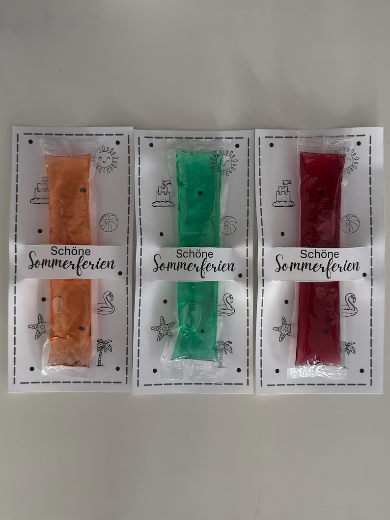 Puede incluir: Tres bolsas selladas de golosinas congeladas, naranja, verde y rojo, se exhiben en tarjetas blancas. Cada tarjeta tiene un borde decorativo y el texto alem&aacute;n "Sch&ouml;ne Sommerferien". Las tarjetas presentan ilustraciones tem&aacute;ticas de verano.