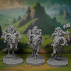 May include: Three gray miniature figurines of female warriors riding rams. Each figure is in a different pose, one holding a hammer, another a shield, and the third a block. The background features a blurred green landscape.
