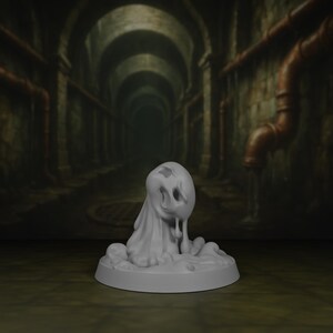 Op de afbeelding: Een grijze, 3D-geprinte miniatuur van een spookachtig wezen. De figuur heeft een afgeronde kop met oog- en mondopeningen en een gedrapeerd, vloeiend lichaam. Het staat op een cirkelvormige basis.