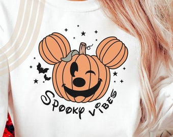May include: White sweatshirt with a pumpkin-shaped Mickey Mouse head design. The pumpkin has a winking face and the text "Spooky Vibes" is printed below it.