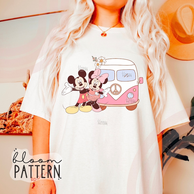 May include: White t-shirt with a graphic of Mickey Mouse and Minnie Mouse standing in front of a pink and white vintage van with flowers and a peace sign. The text "bloom pattern" is on the shirt.
