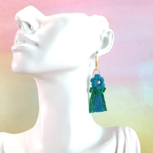 May include: Teal and green tassel earrings with a flower charm and a gold hook.