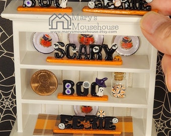 May include: A white hutch with three shelves decorated with Halloween themed items. The top shelf has the words "BOO" and "EERIE" in black letters with orange accents. The middle shelf has the words "SCARY" in black letters with orange accents and two plates with a pumpkin design. The bottom shelf has the words "BOO" and "EERIE" in black letters with orange accents. The hutch has two drawers and a black spider on the bottom shelf.
