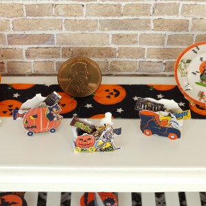 May include: A miniature Halloween display featuring a small orange plastic jack-o'-lantern bucket, a US penny for scale, and a decorative plate. Several small paper cutouts of pumpkins, a skeleton, and a shoe are filled with miniature candy bars.