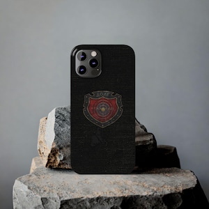 May include: Black phone case with a textured finish. The case features a shield emblem with the Greek letters ΔΟΛΓ in gold. The shield has a red and gold design with a target-like centre.