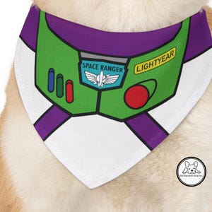 May include: A white dog bandana featuring a green and purple design inspired by Buzz Lightyear's spacesuit. The bandana includes the text "SPACE RANGER" and "LIGHTYEAR". The design has red, blue, and green accents.