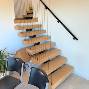 Może przedstawiać: Nowoczesne drewniane schody z czarną metalową poręczą i systemem balustrad linowych. Schody są zawieszone na suficie i mają elegancki, współczesny design.