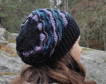 May include: A black, blue, and purple knitted beanie with a swirling pattern. The beanie is worn by a person with long brown hair.