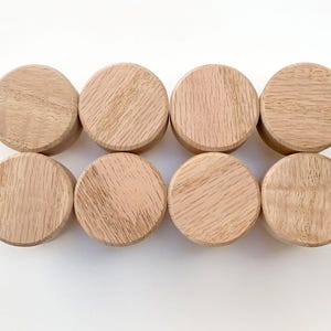 May include: Eight circular wooden knobs arranged in two rows of four. Each knob features a light brown natural wood grain pattern with a smooth, flat top surface and a cylindrical shape, showcasing the organic texture of the wood material.