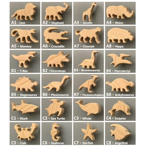 K&ouml;nnte beinhalten: Eine Sammlung von hellbraunen Holzfiguren in Form von Tieren und Dinosauriern, angeordnet in einem Raster. Jede Figur ist mit einem Code und Namen beschriftet, darunter L&ouml;we, Elefant, Giraffe, Nashorn, Affe, Krokodil, Gepard, Nilpferd, T-Rex, Triceratops, Brontosaurus, Pterodactylus, Stegosaurus, Plesiosaurus, Parasaurolophus, Ankylosaurus, Hai, Meeresschildkr&ouml;te, Wal, Delfin, Krabbe, Seepferdchen, Seestern und Kaiserfisch.