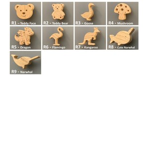 K&ouml;nnte beinhalten: Eine Sammlung von neun hellen Holzhaken in Form von Tieren und Naturmotiven, beschriftet von R1 bis R9. Die Designs umfassen ein B&auml;rengesicht, einen Teddyb&auml;ren, eine Gans, einen Pilz, einen Drachen, einen Flamingo, ein K&auml;nguru und zwei Narwale.