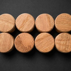 May include: Eight circular wooden knobs arranged in two rows of four. Each knob features a natural light brown wood grain pattern with a smooth, flat top surface and a cylindrical shape, showcasing the distinct texture and colour of the wood.
