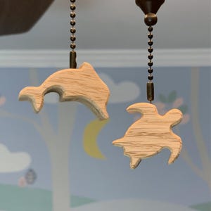 May include: Two wooden fan pull chains, one shaped like a dolphin and the other shaped like a sea turtle.