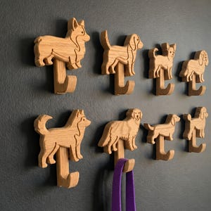May include: A collection of wooden dog-shaped hooks mounted on a gray wall. The hooks are carved in various dog breeds, including a Corgi, Husky, and Golden Retriever. A purple leash hangs from one hook.