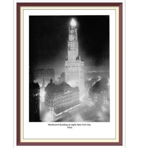 May include: A black and white photograph of the Woolworth Building in New York City at night, illuminated by lights. The building is tall and slender, with a pointed top. The photo was taken in 1913.